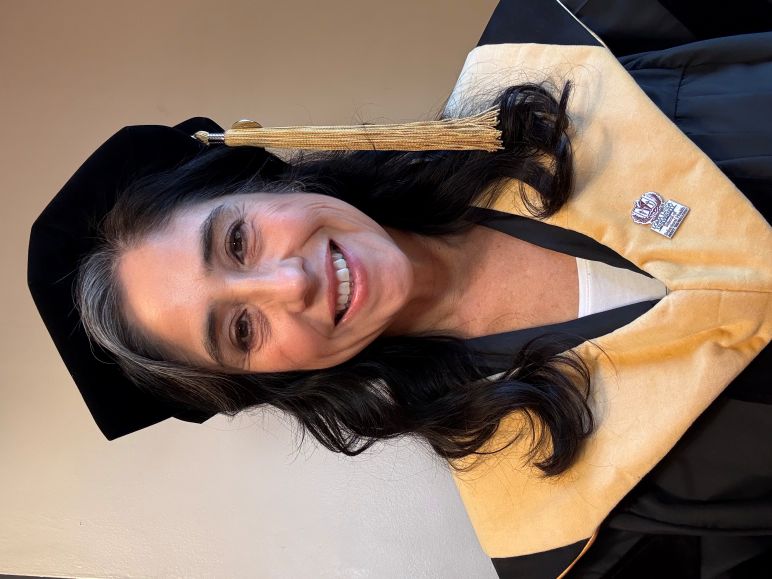 Dr. Kelley Martinez smiles at the camera, wearing full academic regalia.