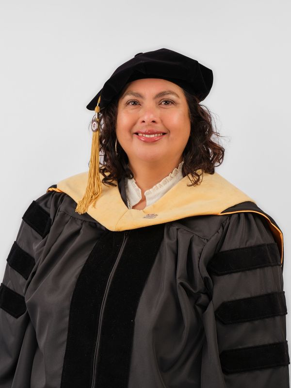 Dr. Mary Lopez-Inayama smiles at the camera, wearing full academic regalia.