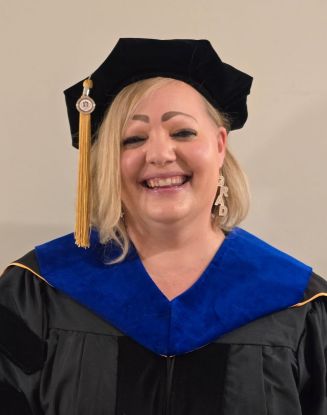 Dr. Sarah Beaver smiles at the camera, wearing full academic regalia.