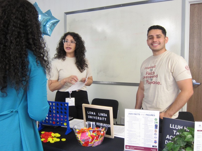 Two Loma Linda University Human Resources representatives speak with a student at their booth during the 2026 SBH Job Fair. The table displays a Connect Four game, candy, and informational materials including a 2025 Facts and Figures sheet.