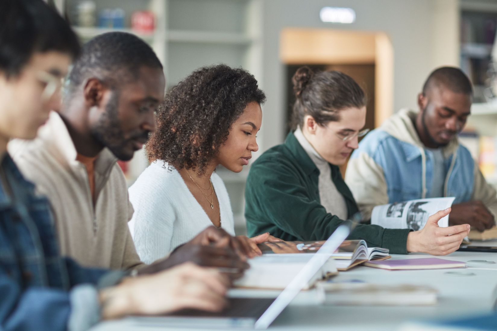 A group of graduate students studying together at a library table, reading and taking notes as they prepare for doctoral training.