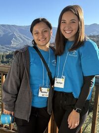 Ashley Gonzalez and Kaitlyn Saunders, Loma Linda University Child Life Specialist MS students, smile on a wooden deck overlooking a mountain landscape during Camp Good Grief.