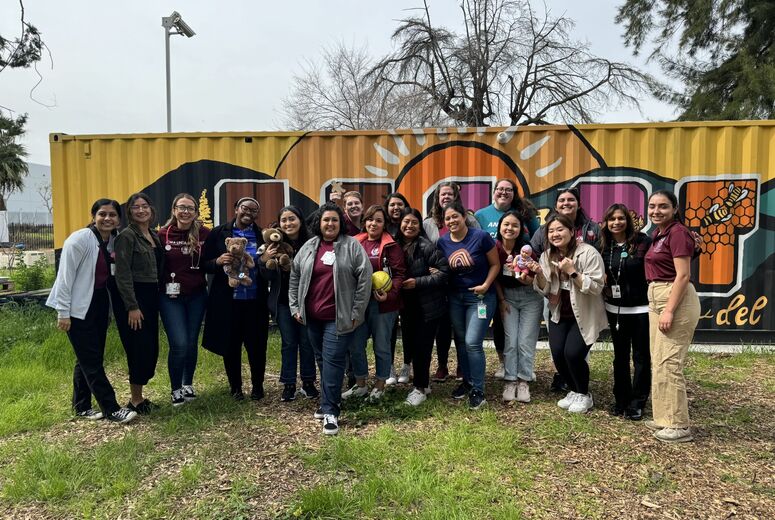 Child Life students and faculty standing together on a lawn in front of what appears to be a graffiti-style painted shipping container