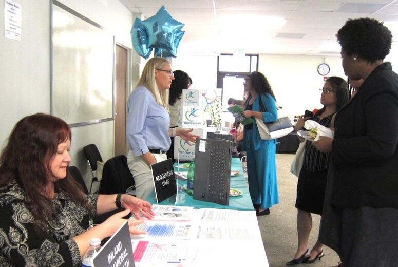 Students browse employer tables at the 2026 SBH Job Fair, stopping to speak with representatives from Inland Behavioral Health Services and NeoGenesis Care. Teal star-shaped balloons decorate the booths.