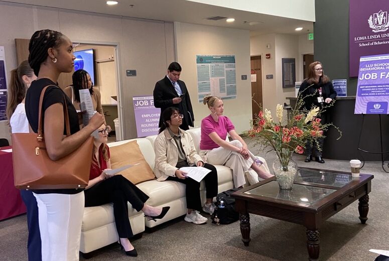 Students gather in the lobby of the job fair venue, some seated on a couch reviewing materials and others standing. LLU School of Behavioral Health Job Fair signage and an employer/alumni roundtable discussion sign are visible in the background.