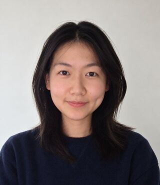 Portrait of Counseling MS student Julie Ma with shoulder-length dark hair parted in the center, wearing a navy sweater and a soft, closed-mouth smile, photographed in front of a plain white wall.
