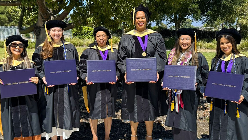 smiling graduates in regalia holding diplomas