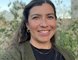 Headshot of Dr. Danielle Lascano smiling outdoors, wearing an olive green cardigan over a black top, with greenery in the background.