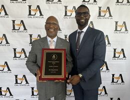 Dr. Craig Jackson and Dr. Maurice Hudson stand together in front of a logo step and repeat background, smiling at the camera. Dr. Jackson, on the left, is holding an award. Both are wearing suits and ties.