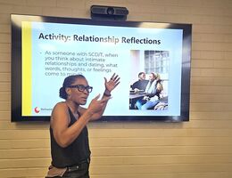 Dr. Monique Willis presenting a slide titled 'Activity: Relationship Reflections' during a talk on relationships and dating for people with sickle cell disease and trait, with a photo of a couple smiling together displayed on screen.