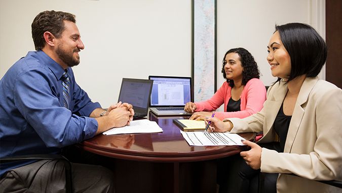 faculty member talking with two female students at his desk